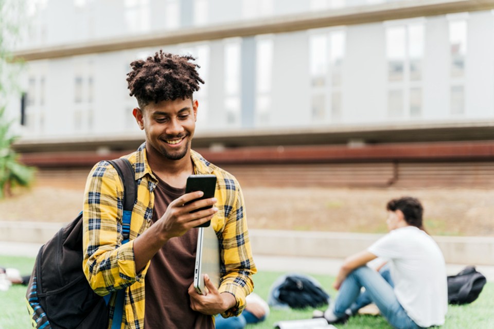 Male student walking outside using phone and smiling