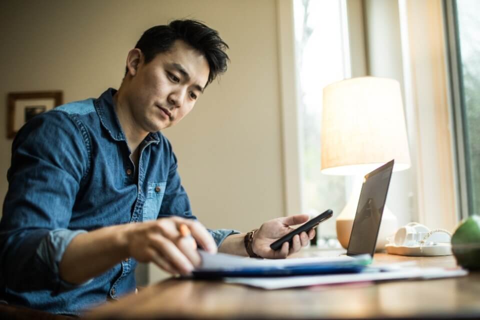 Male professional with phone and laptop sitting at desk looking at papers