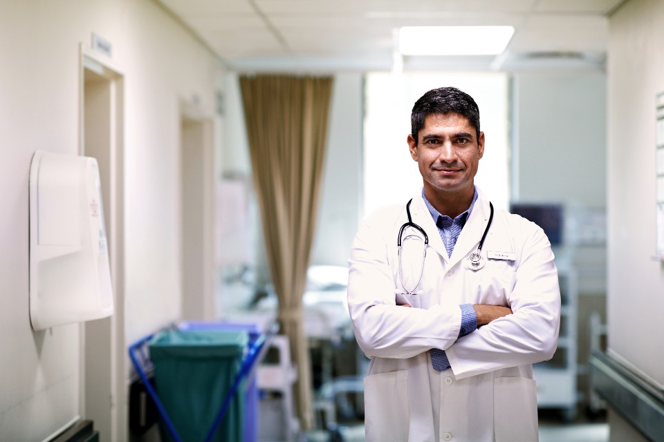 Mature male doctor standing in consultation room with crossed arms