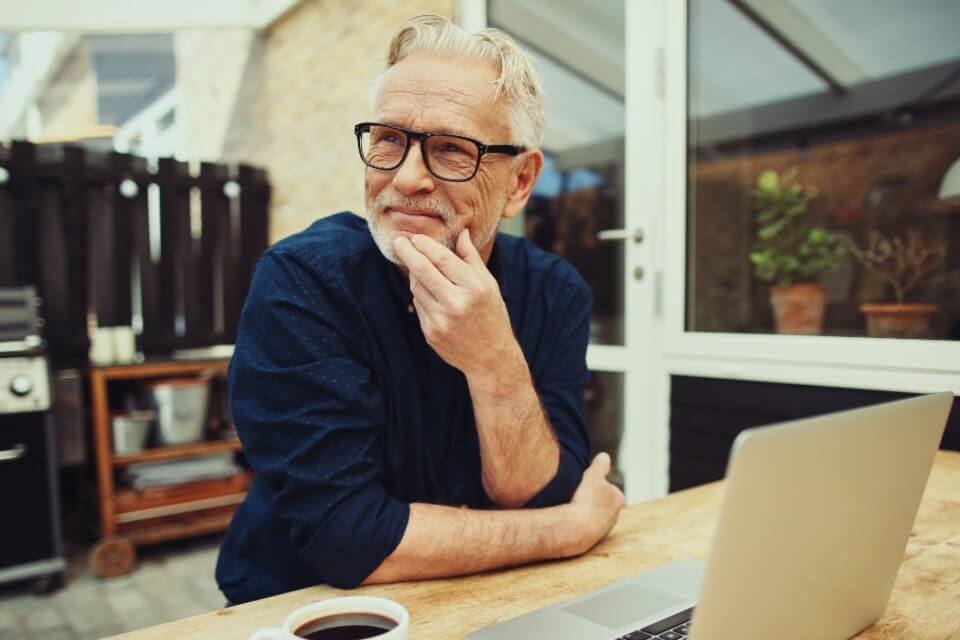 Mature man sitting on table with laptop and coffee