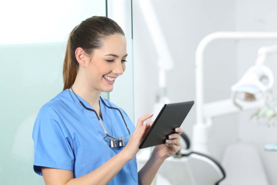 Female dentist in scrubs looking at tablet while smiling