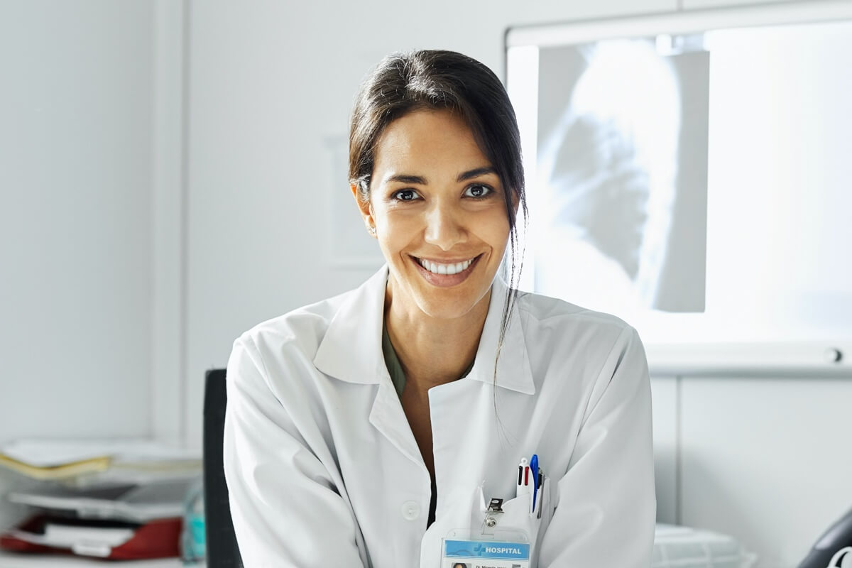 Female doctor wearing a white coat in consultation room sitting at a desk