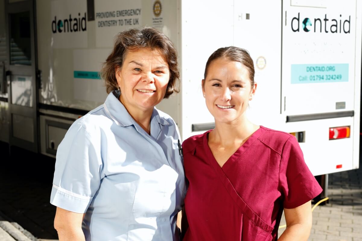 Two nurses in scrubs stand in front of Dentaid van