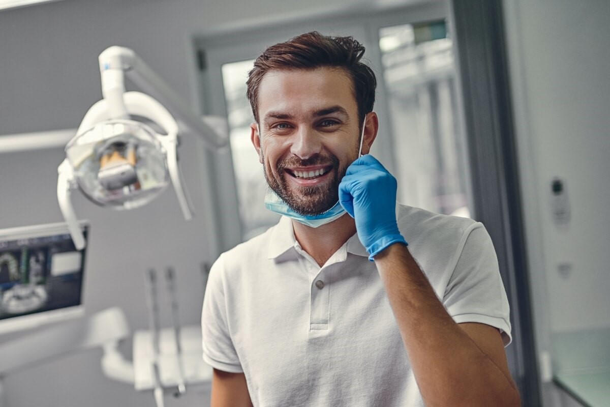 Young male dentist pulling down a mask and smiling in dental room