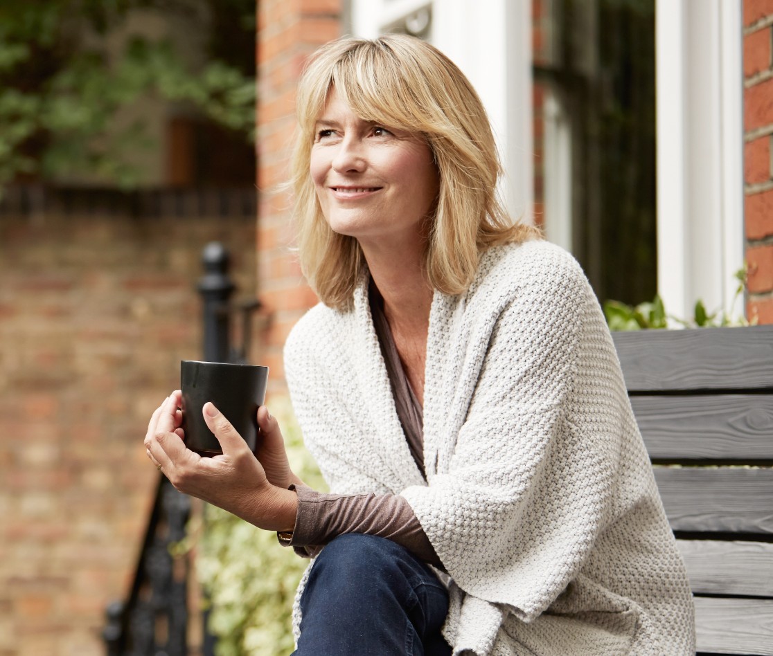 Female sitting outside smiling and holding a mug