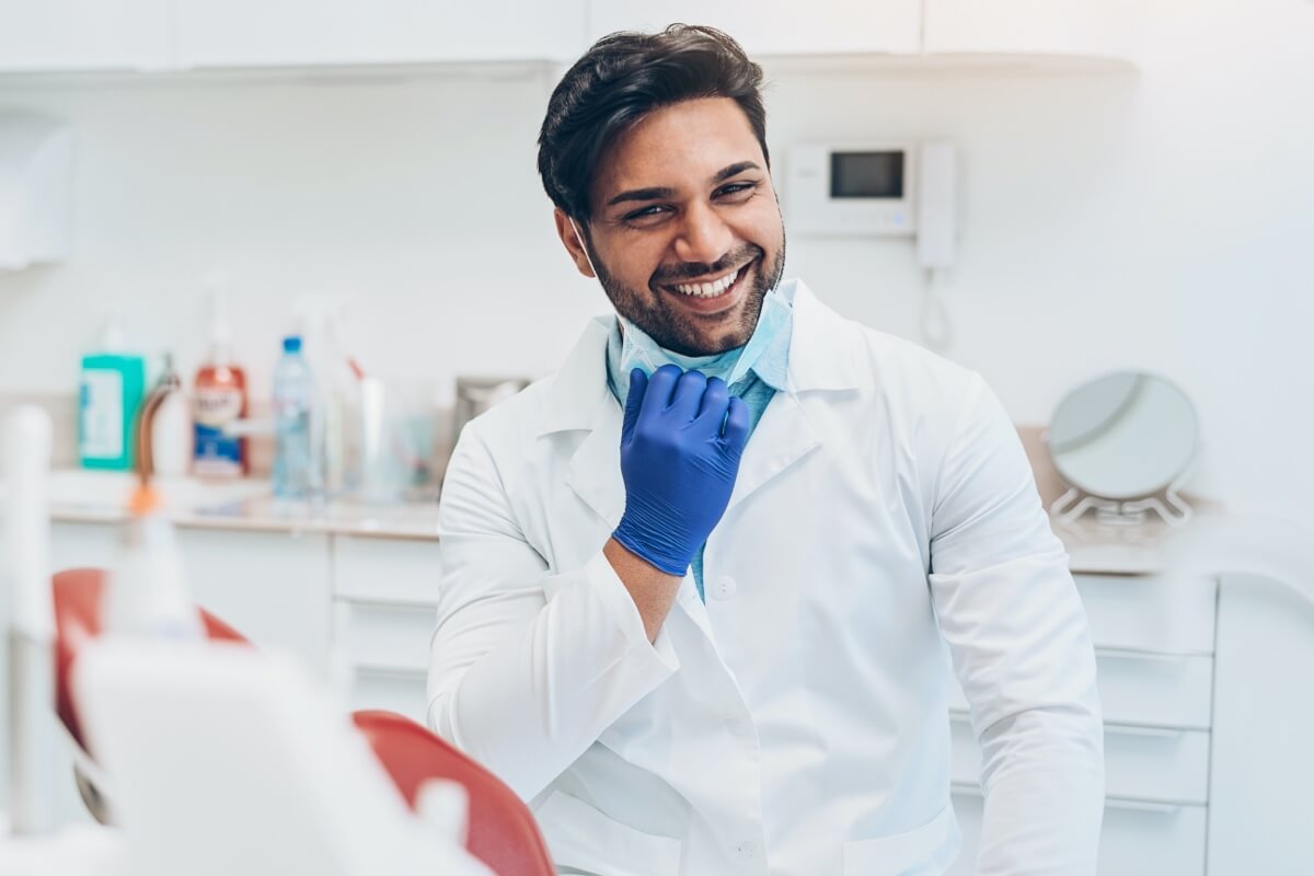 Male dentist pulling mask down smiling