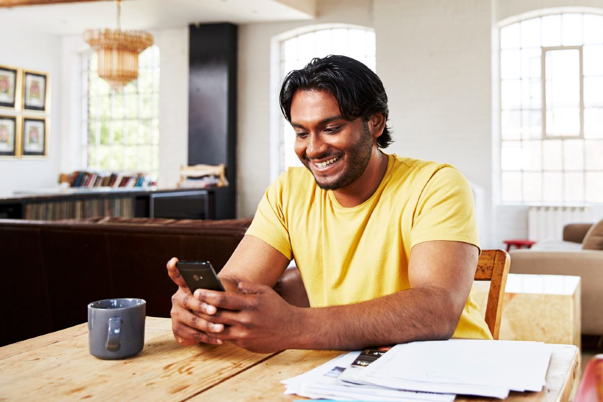 Male sitting at table with papers using phone smiling