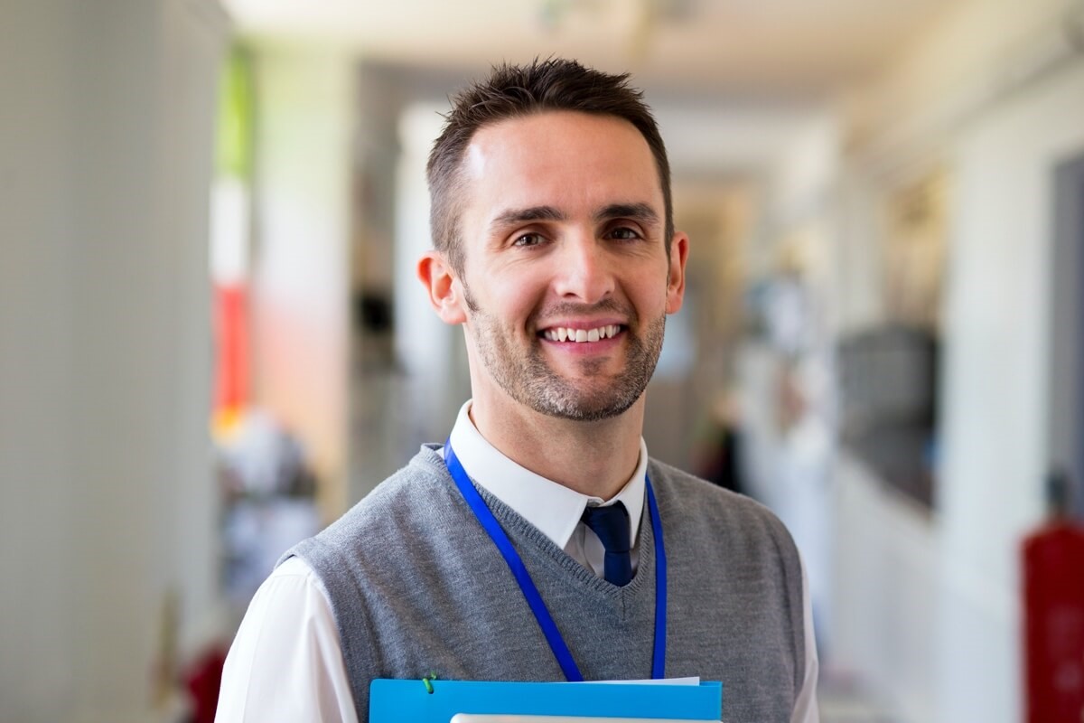 Male teacher smiling holding files