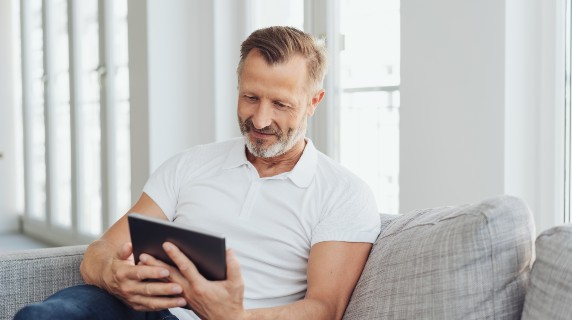 Mature man sitting on sofa holding ipad