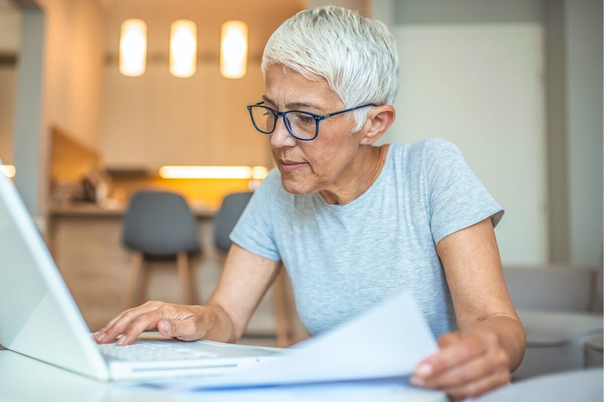 Mature woman on laptop and looking at papers