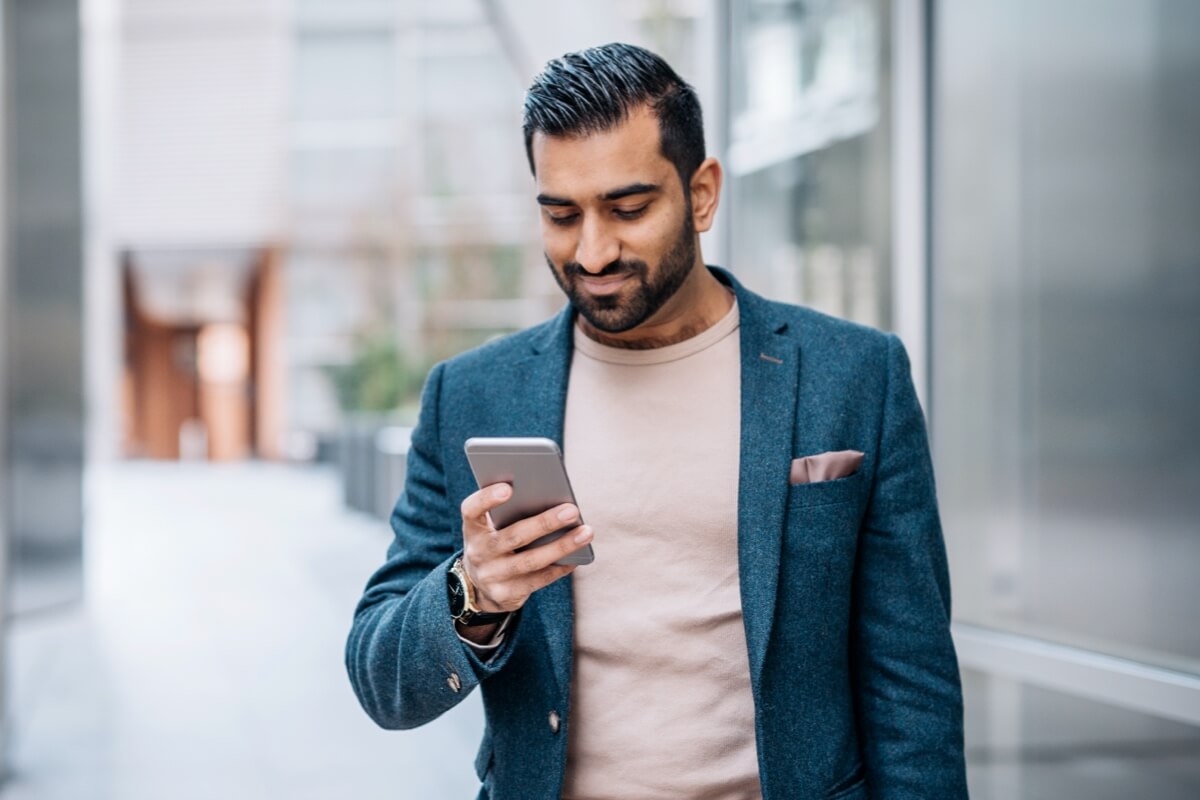 Smartly dressed Asian man smiling down at phone