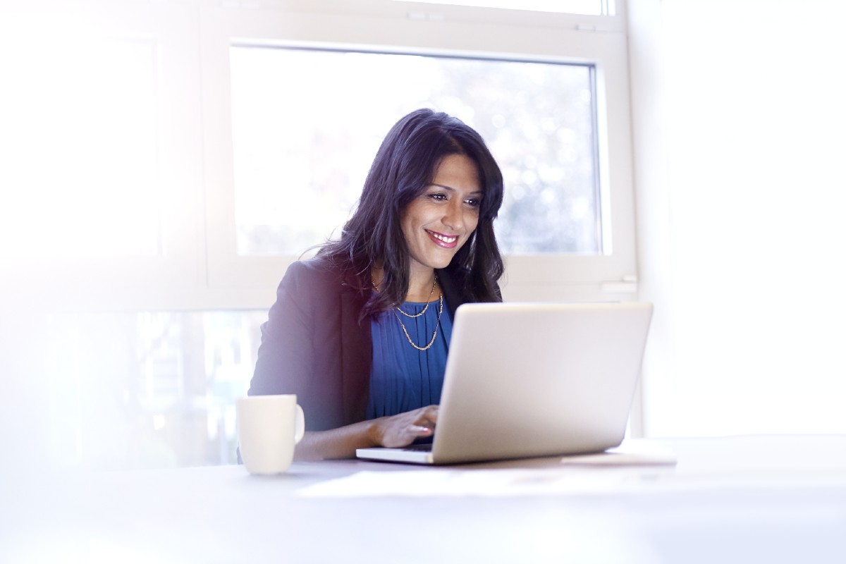 Smartly dressed woman sitting at desk with laptop and mug