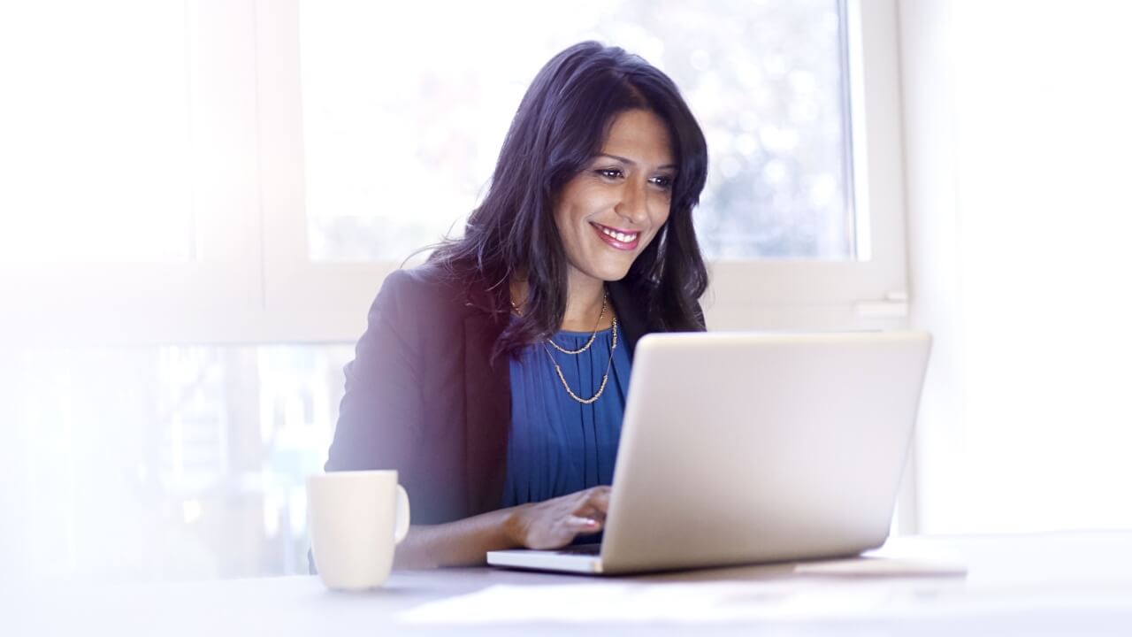 Smartly dressed woman sitting at desk with laptop and mug