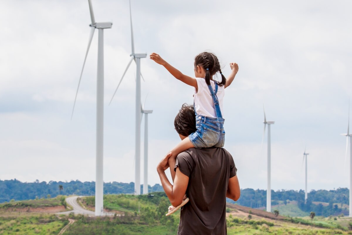 Young child sitting on shoulders in front of wind turbine