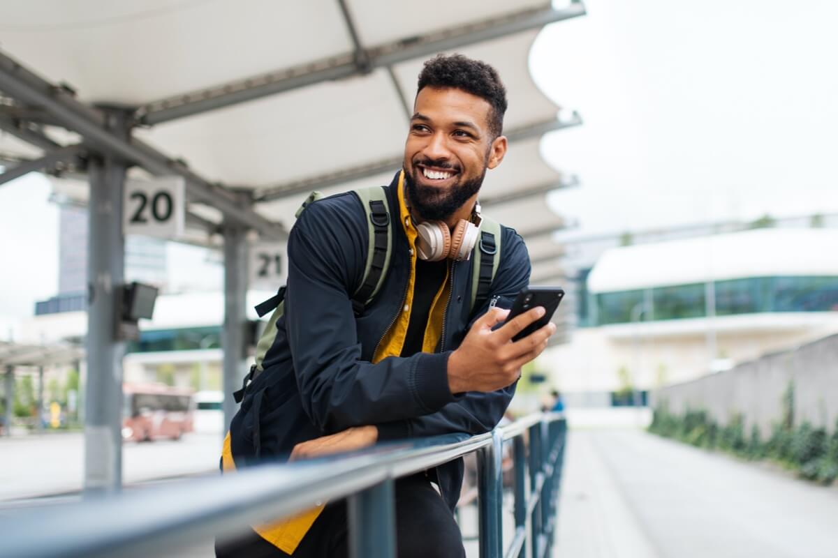 Young man smiling holding phone outdoors