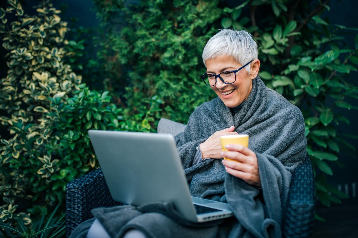 Mature female wearing blanket outside with laptop