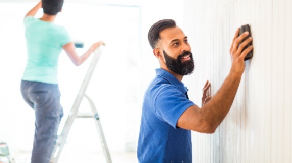 Man sanding down wall