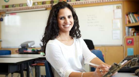 Female teacher sitting in classroom with clipboard