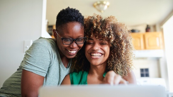 Happy female couple smiling at laptop