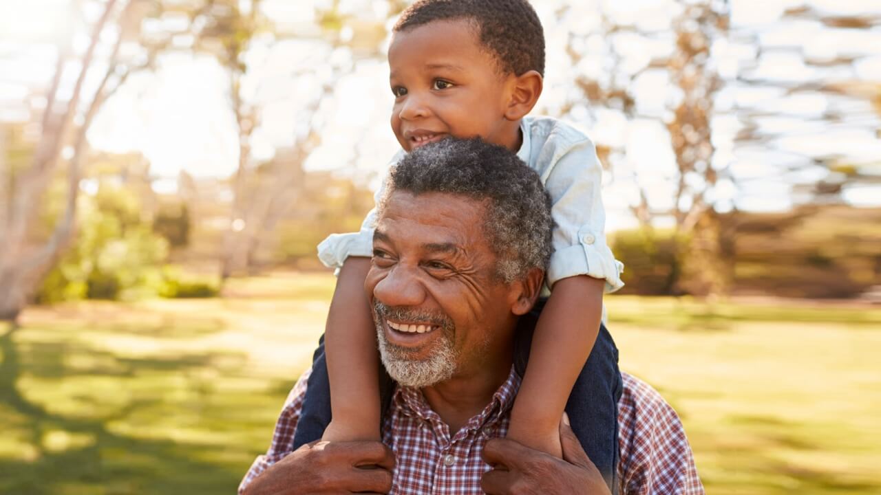 Older man with his grandson on his shoulders in a sunny park