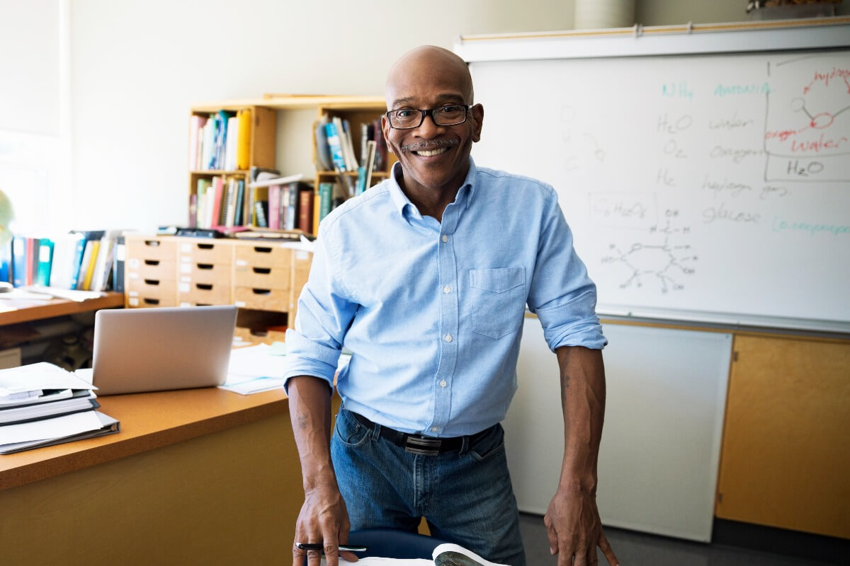 Mature male teacher standing in classroom smiling