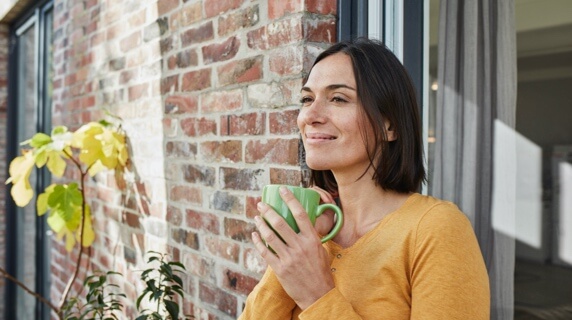 Woman holding mug smiling standing against brick wall