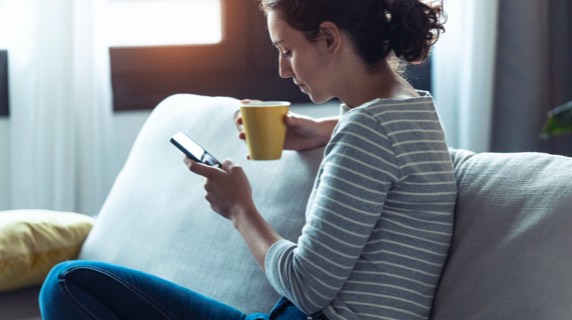 Woman viewing phone and holding mug