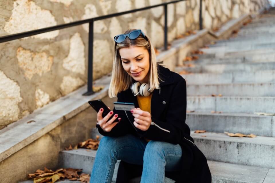 Young woman sitting on step holding phone and bank card