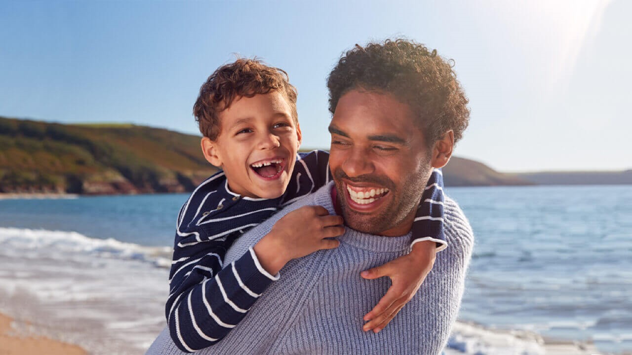 Father giving piggyback to son on beach