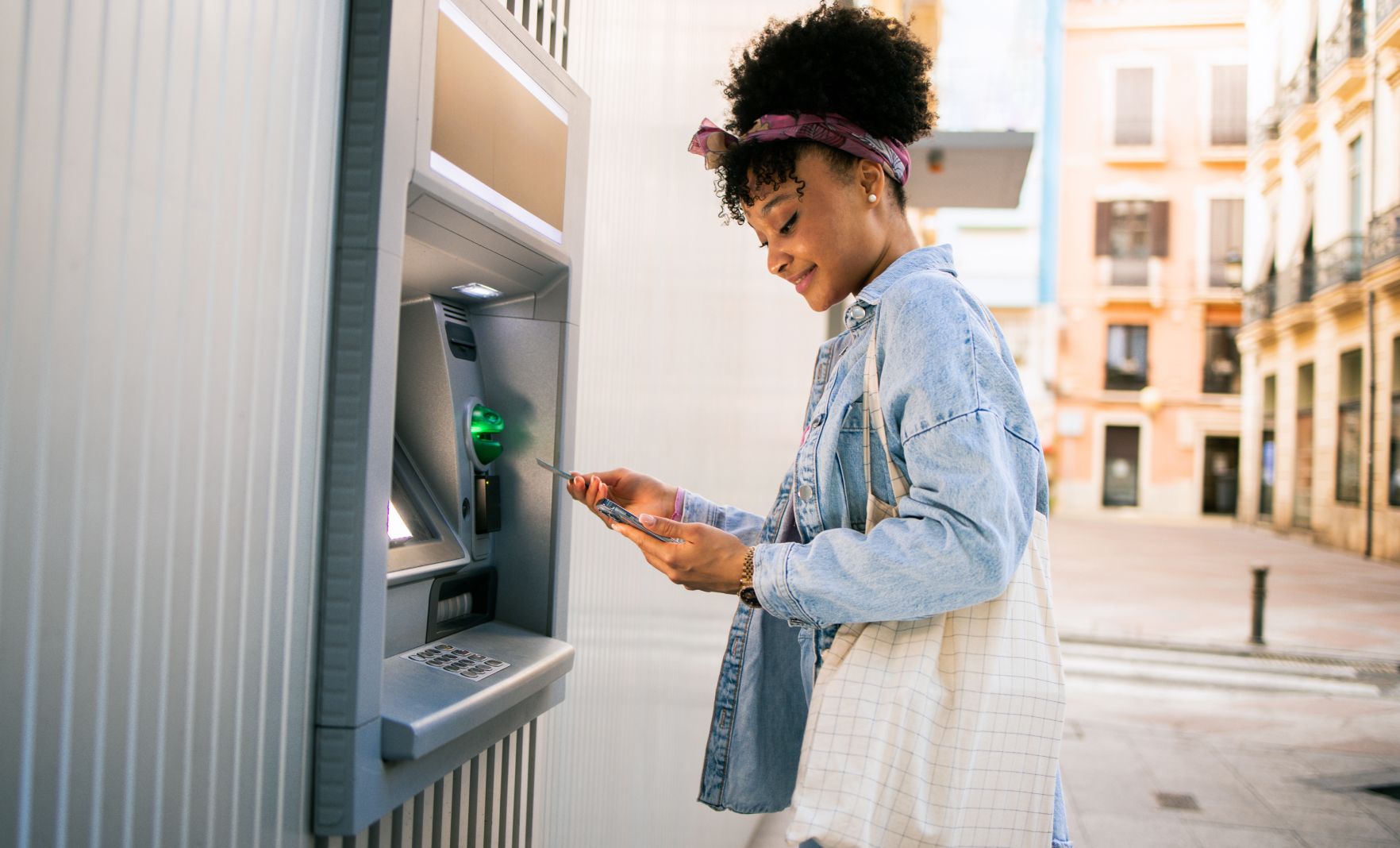 Female at cash machine and looking at her phone