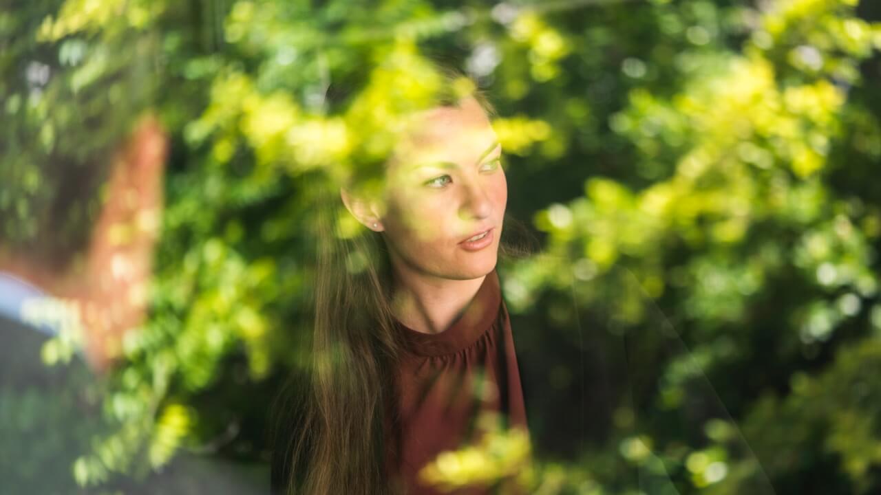 Smartly dressed woman looking out of window with reflections of a tree