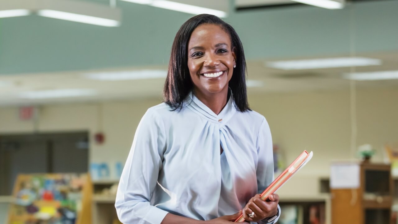 Smiling female teacher holding books in a classroom