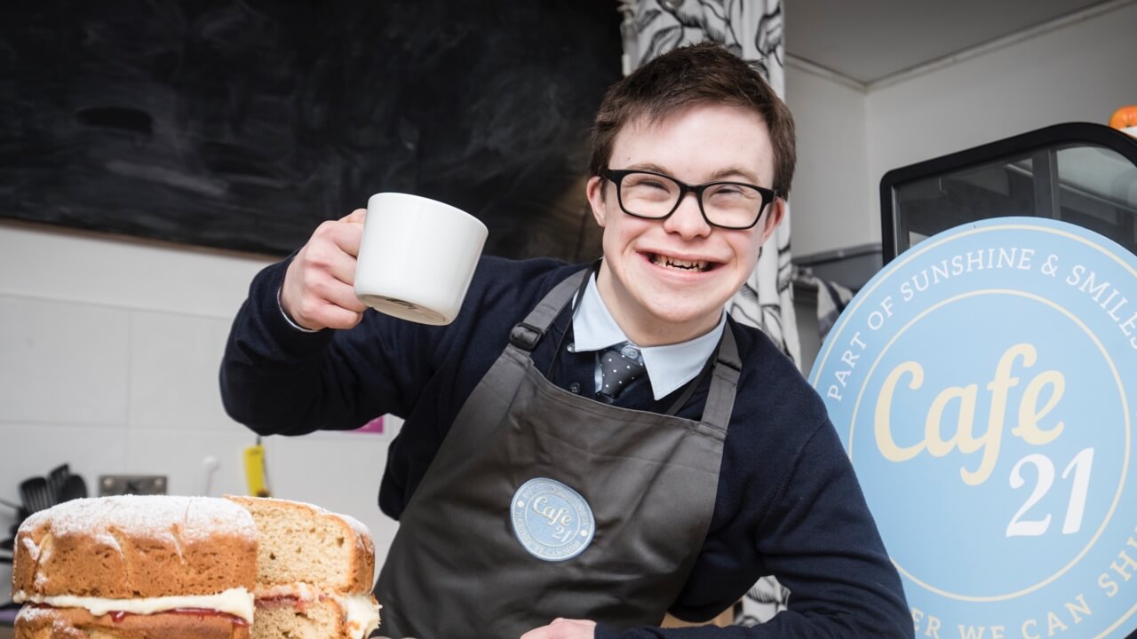 Young child in cafe smiles while holding up a mug