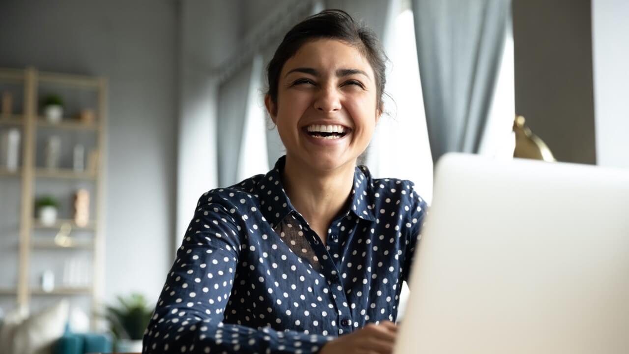 Young professional woman laughing while sat at laptop