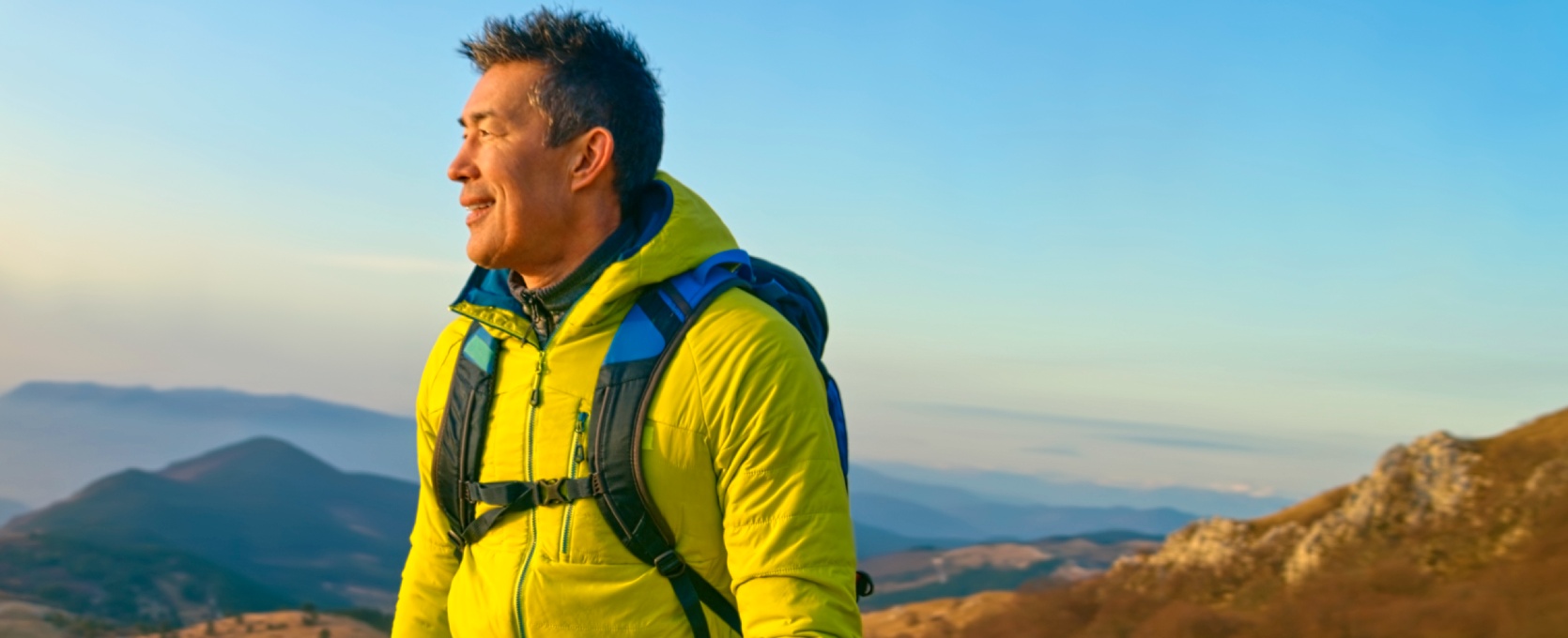 Man in hiking clothes standing on hill looking at sunset