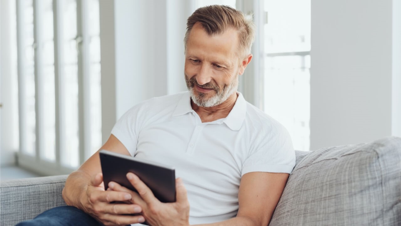 Mature man sitting on sofa holding ipad