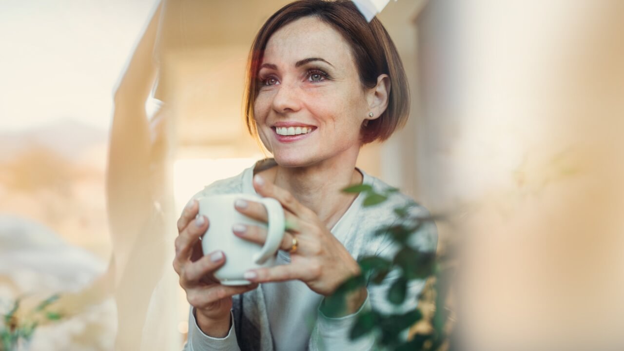 Woman holding mug looking through window