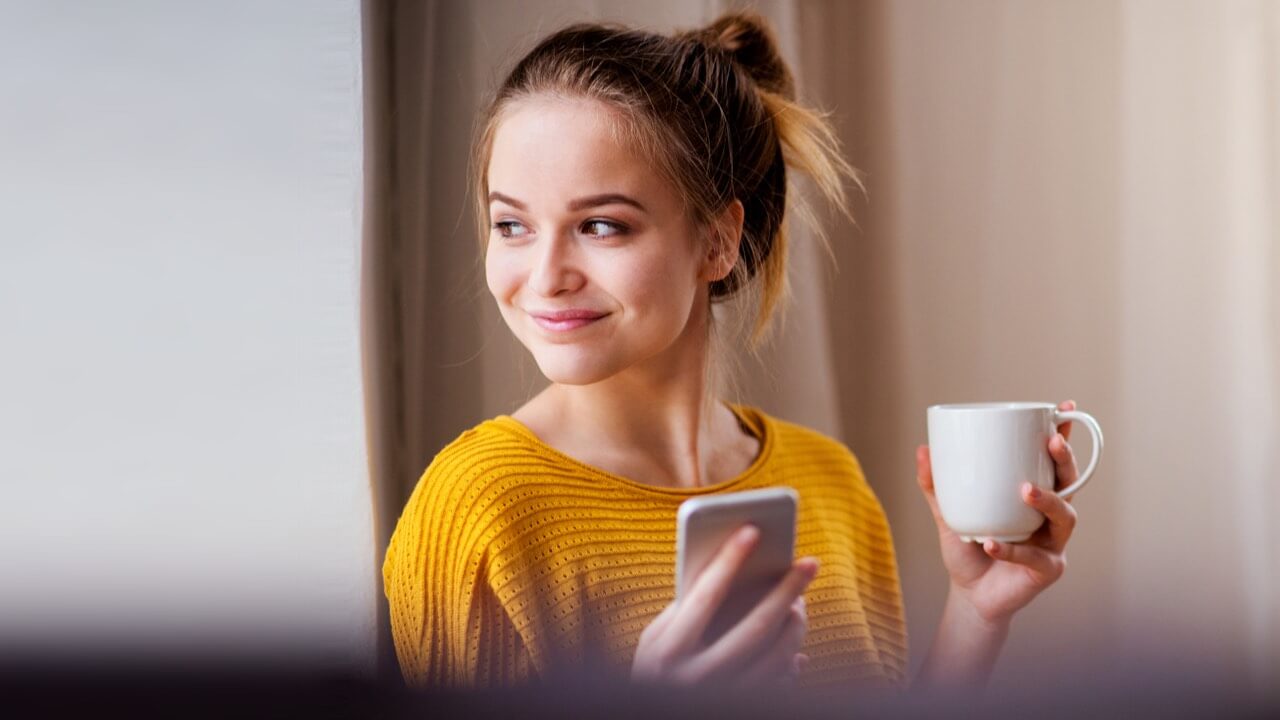 Young woman smiling holding mug and phone