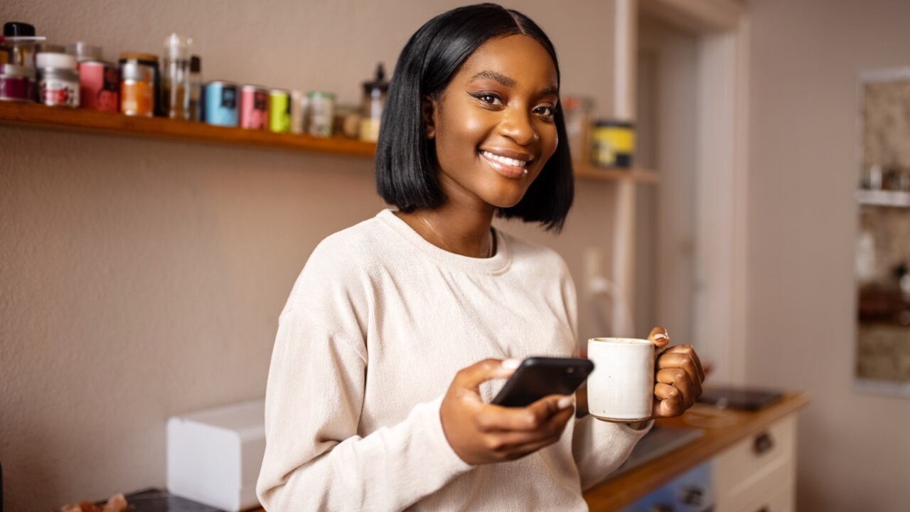 Young woman standing in kitchen smiling using smartphone