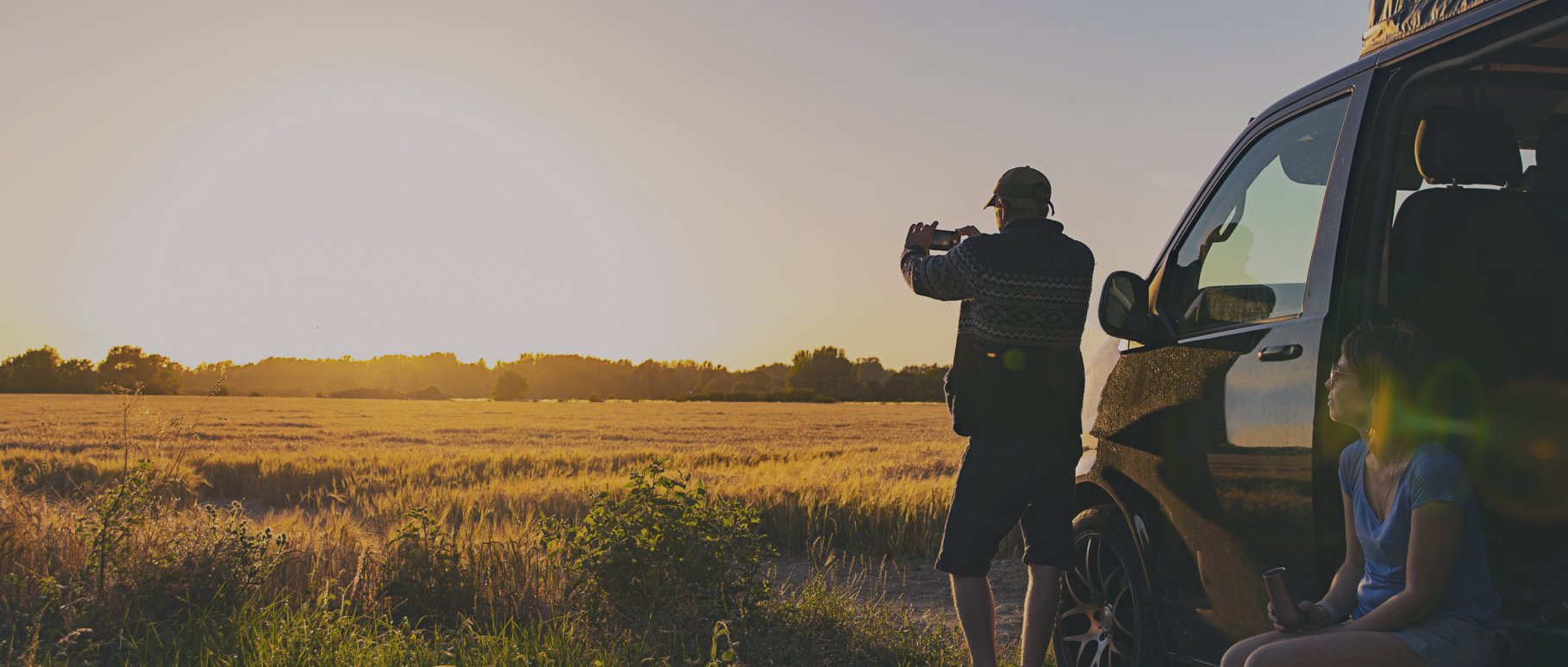 Man taking picture of landscape while woman sits in campervan