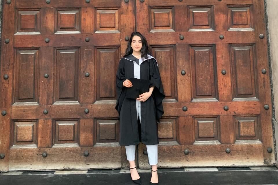 Dr Diana Omar in her graduation gown holding a graduation cap