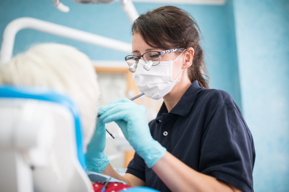 Female dentist wearing mask and glasses treating patient