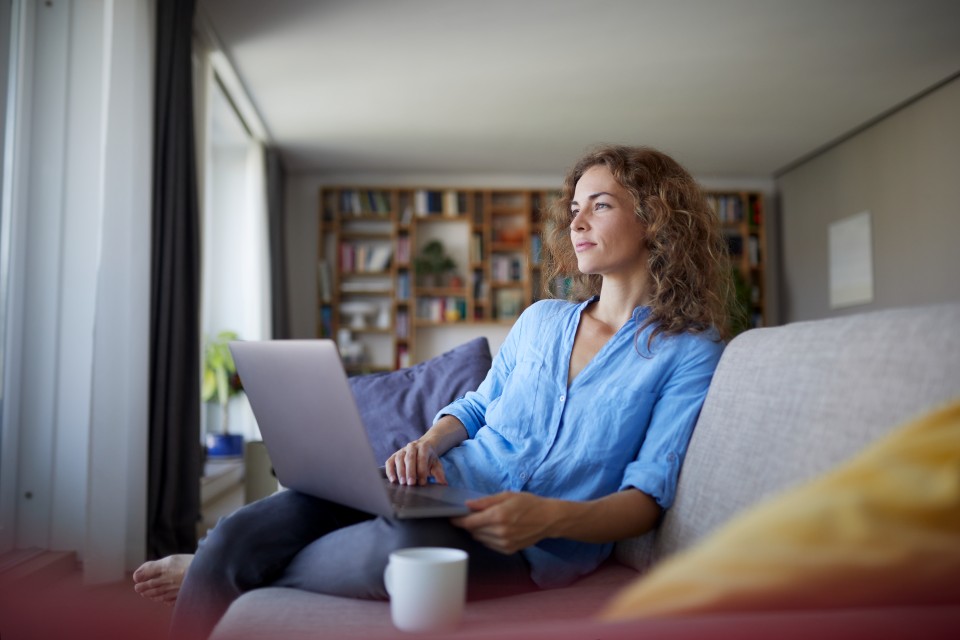 Young woman on sofa with laptop staring out the window