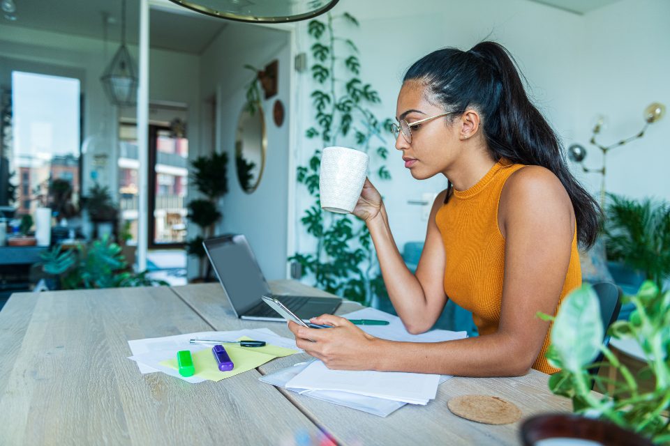 Female student using phone holding mug