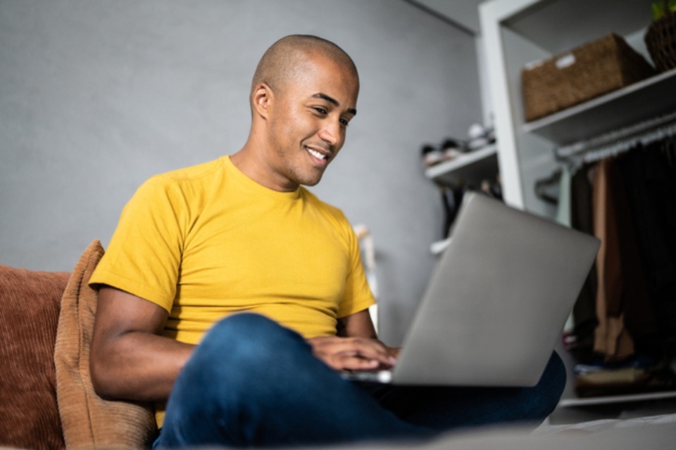 Male student crossed legged with laptop smiling