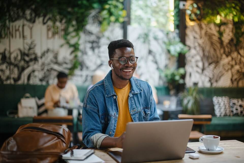 Male student in cafe with laptop smiling