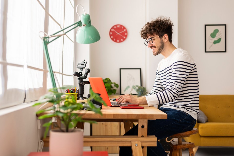 Male student set at wooden desk in home office using a laptop