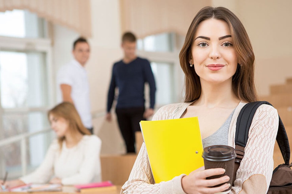 Female student holding yellow notepad and coffee cup