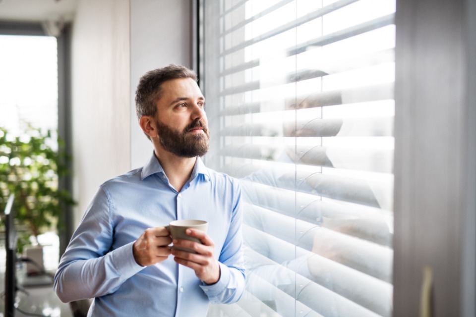 Smartly dressed man holding a mug staring out window