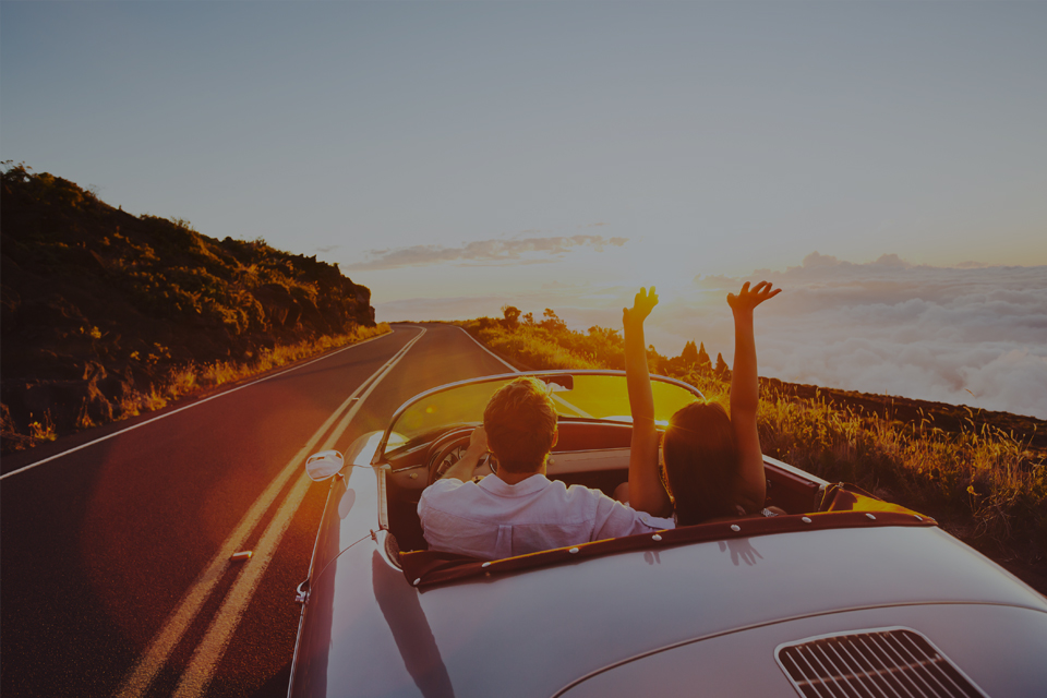 Couple in convertible car driving towards sunset